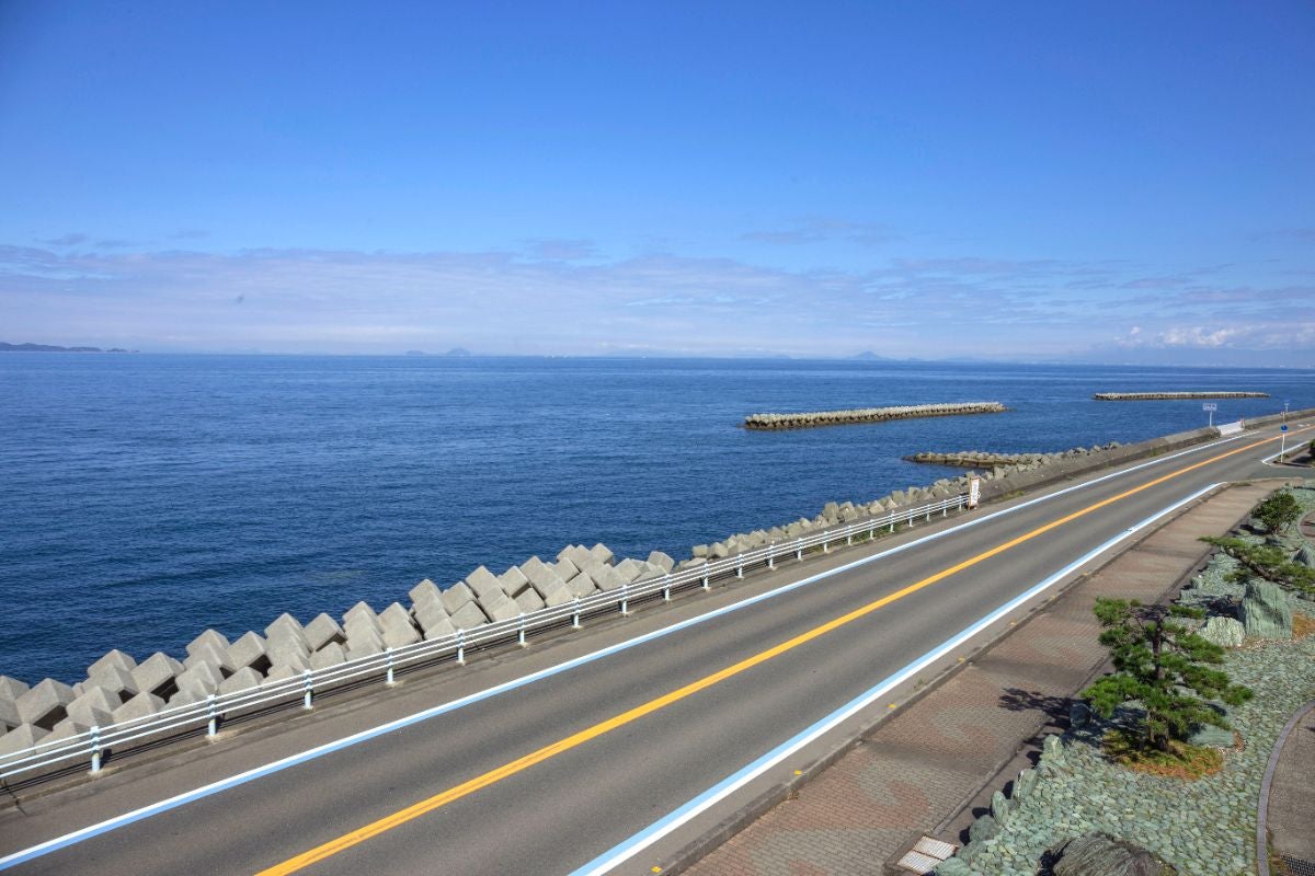 晴天の青空の下、穏やかな海を眺めながら走る国道378号。波消しブロックが並ぶ海岸線沿いに道路が続き、遠くには瀬戸内海の島々がかすんで見える。