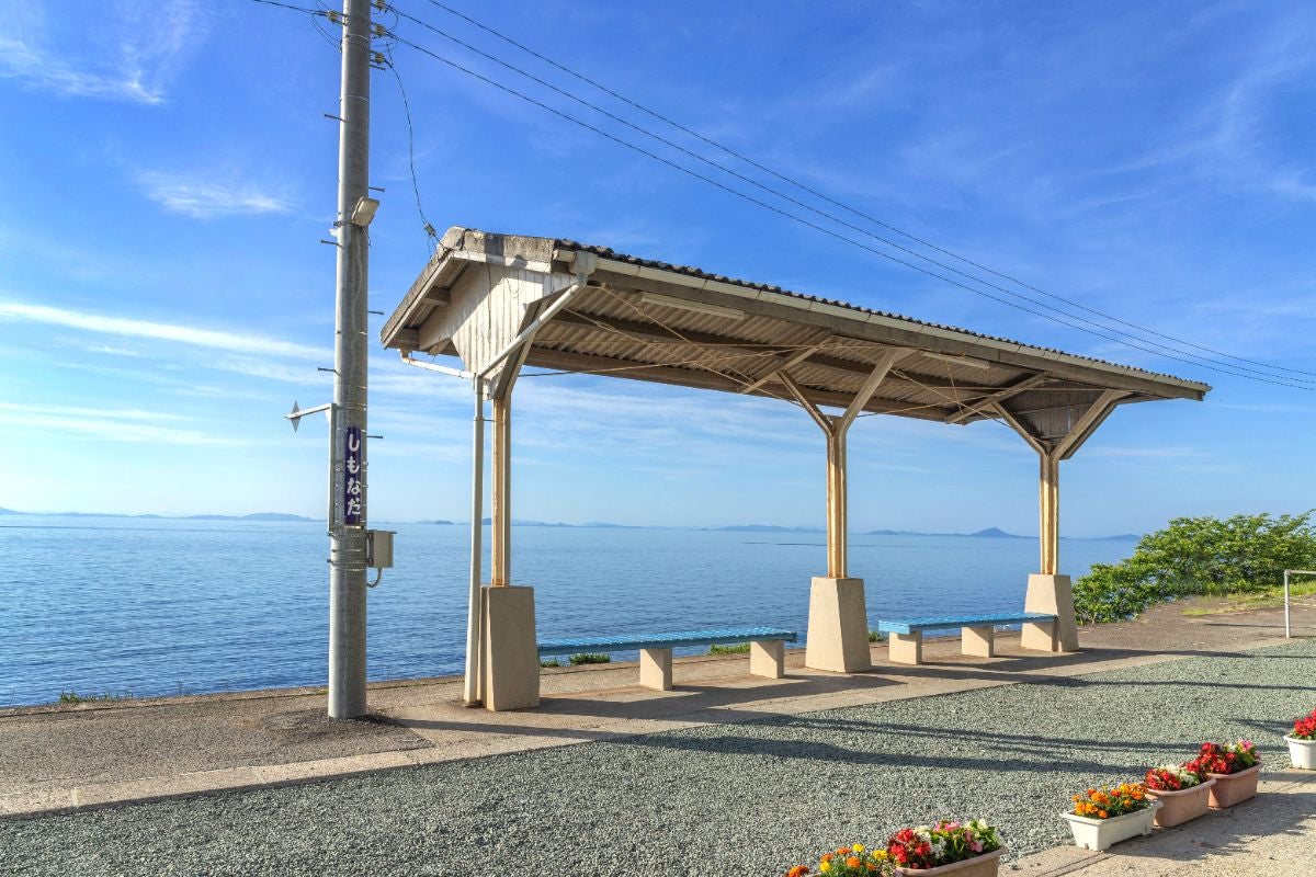 青空と海を背景にたたずむ、JR予讃線・下灘駅のホーム。木造の屋根とベンチがあり、ホームからは瀬戸内海の絶景が一望できる。海と空が一体となったような景色が広がる。