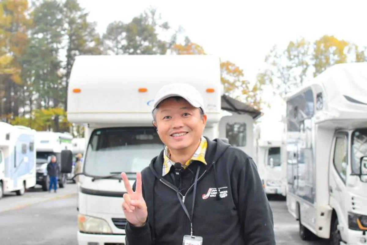 キャンピングカーの前にピースサインする男性