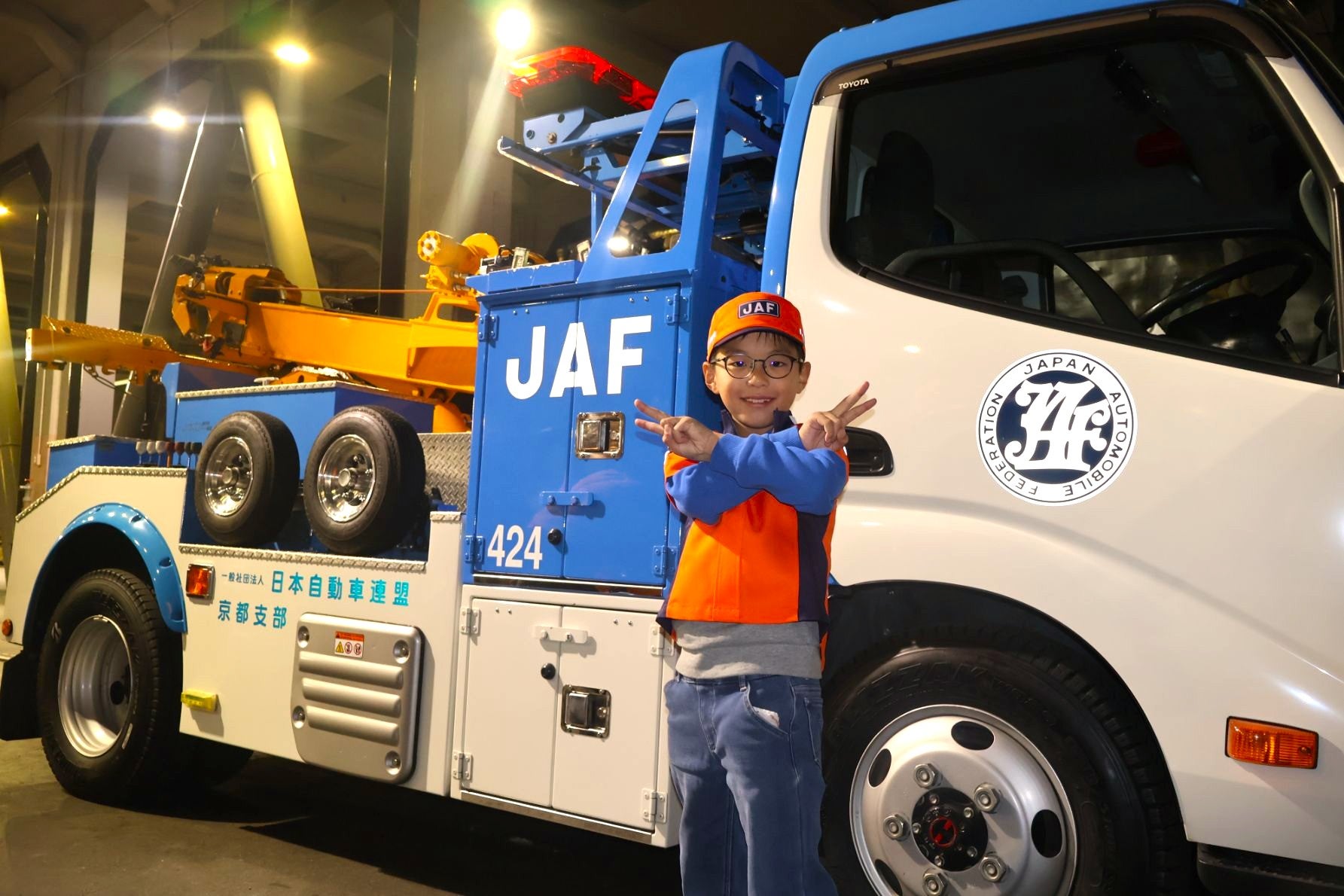 【子ども制服体験】 JAFロードサービス隊員のミニ制服を着用し、展示車両の前で元気にポーズを決める男の子。かっこいい。