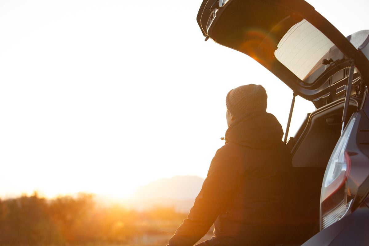 車のトランクを開け、朝日を眺める男性 