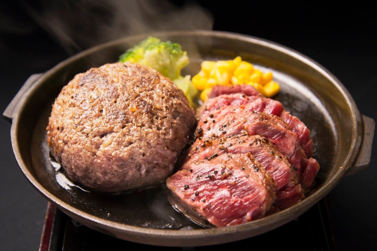 熱々の鉄板に乗ったボリューム満点のハンバーグとスライスされたレアステーキ。ブロッコリーとコーンが添えられてい