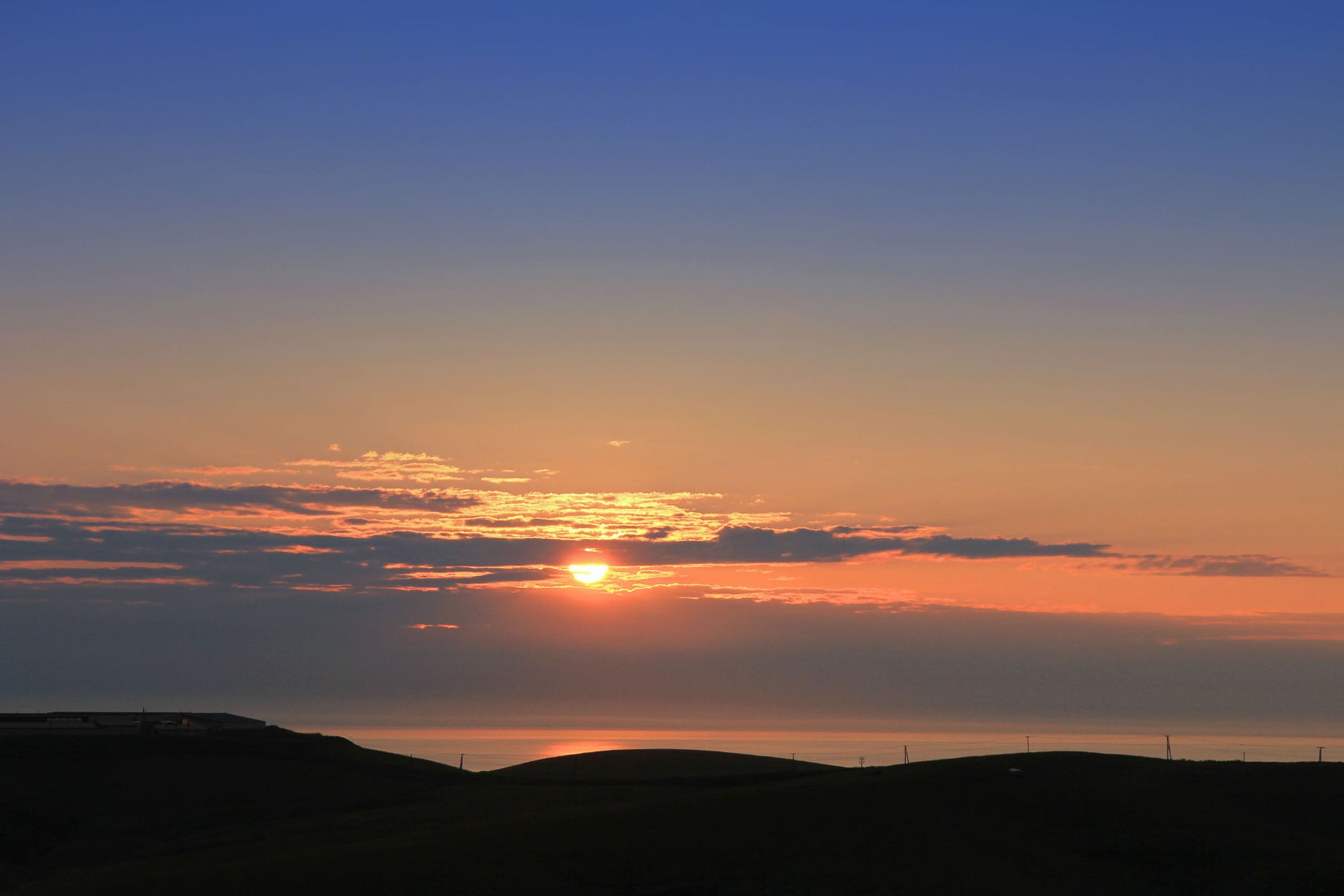 日本海のかなたに静かに沈んでいく夕日。オレンジ色の光が海と空、そして丘陵のシルエットを美しく染め上げる、幻想的なフィナーレだ