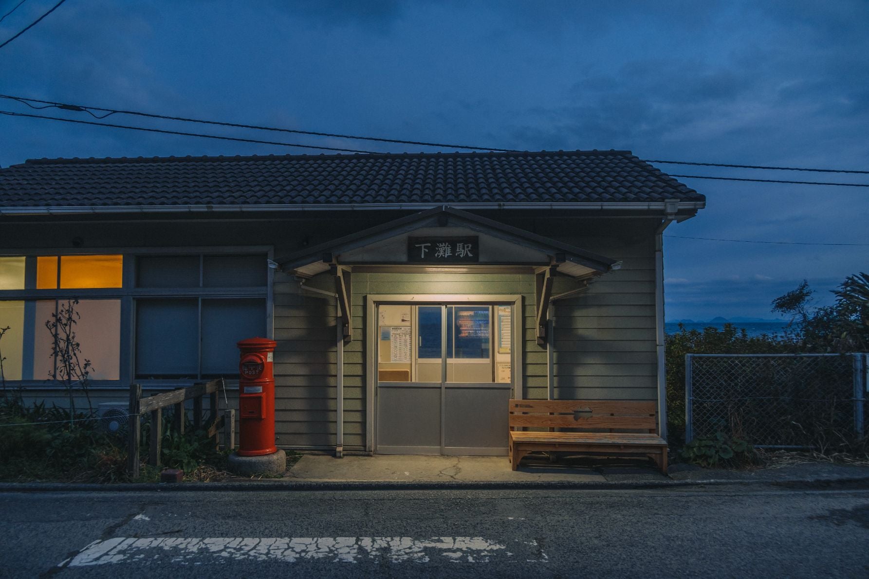 夜明け前の駅舎を照らす明かりと赤い丸ポスト