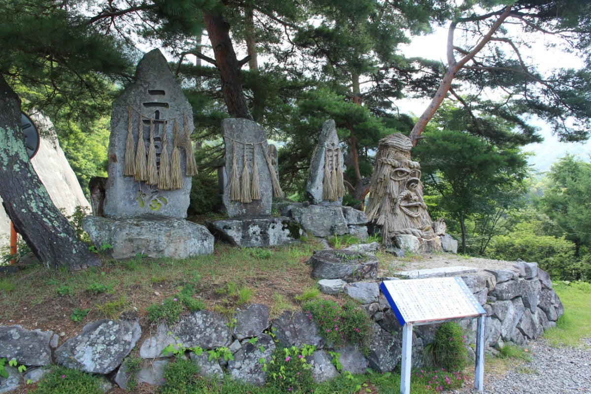 松の木の下に並ぶ、個性的な姿の藁の道祖神たち