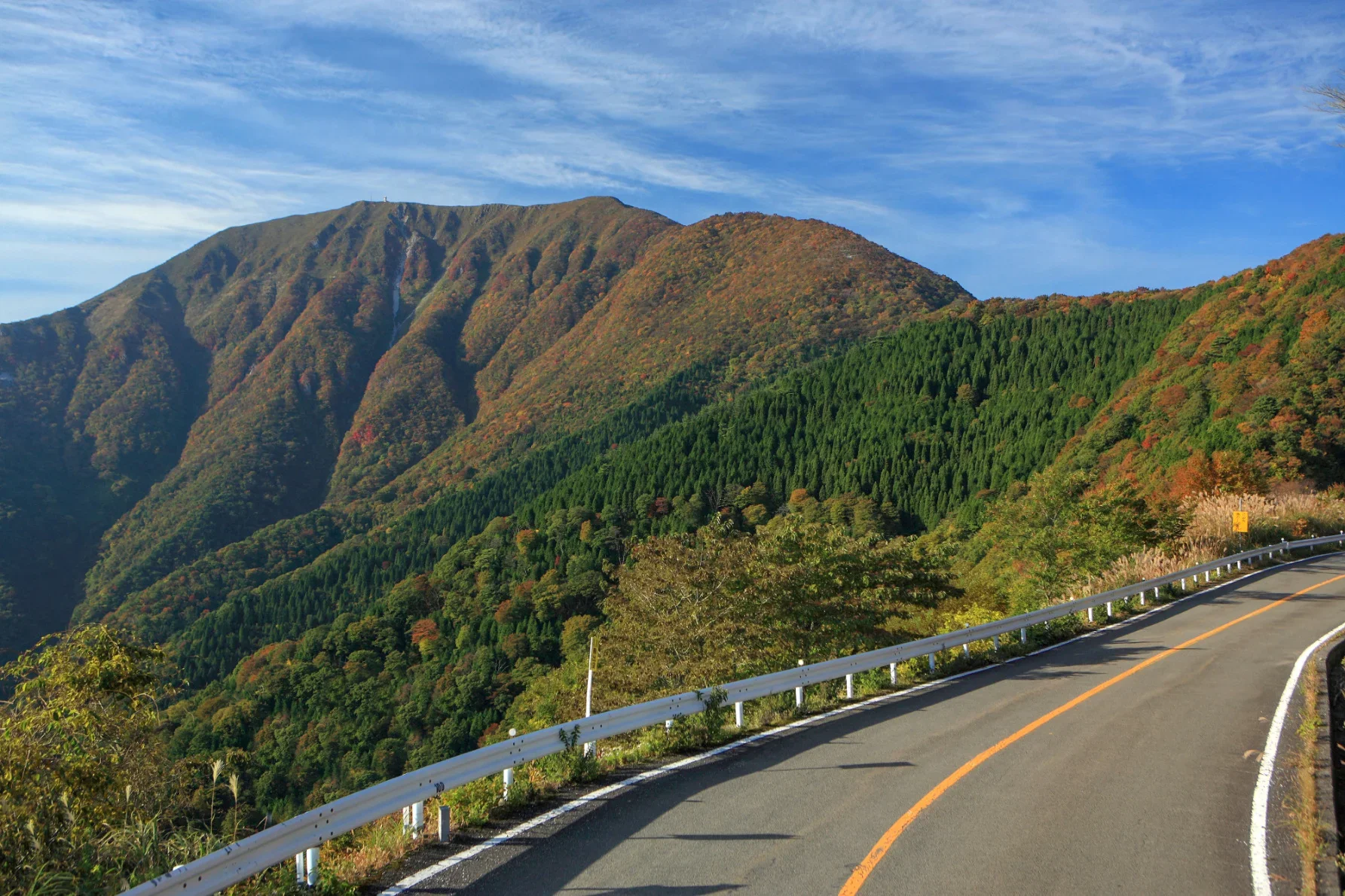 晴れ渡った青空が広がり、遠くには山々が連なる。秋の紅葉が美しく映える山岳道路だ