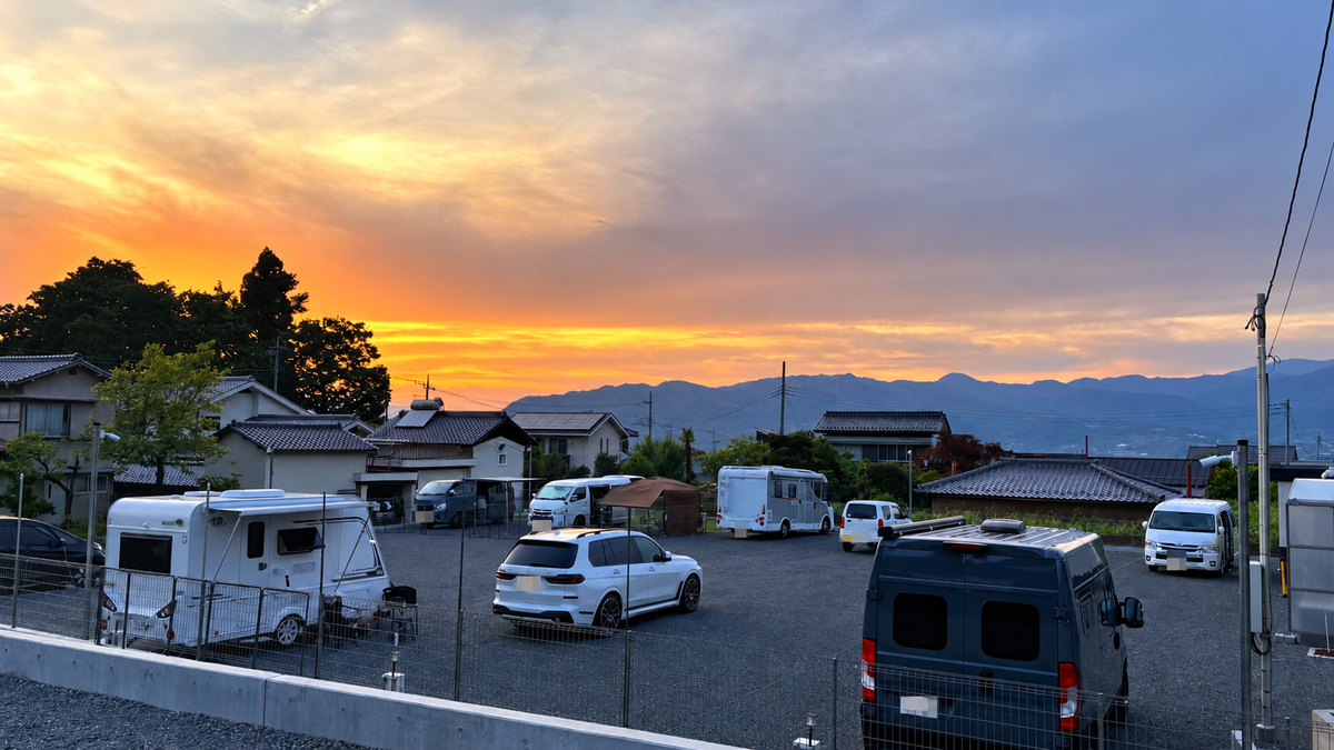 夕景のなか駐車場に停まるキャンピングカーと遠くの山々