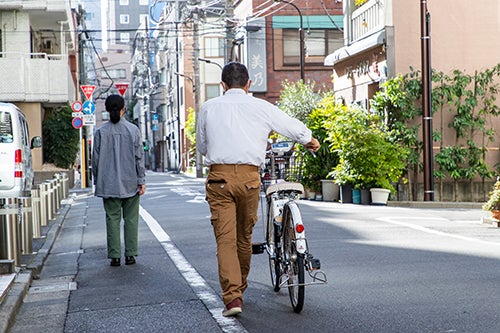 路側帯を歩く女性の後ろを自転車を押しながら歩く男性）