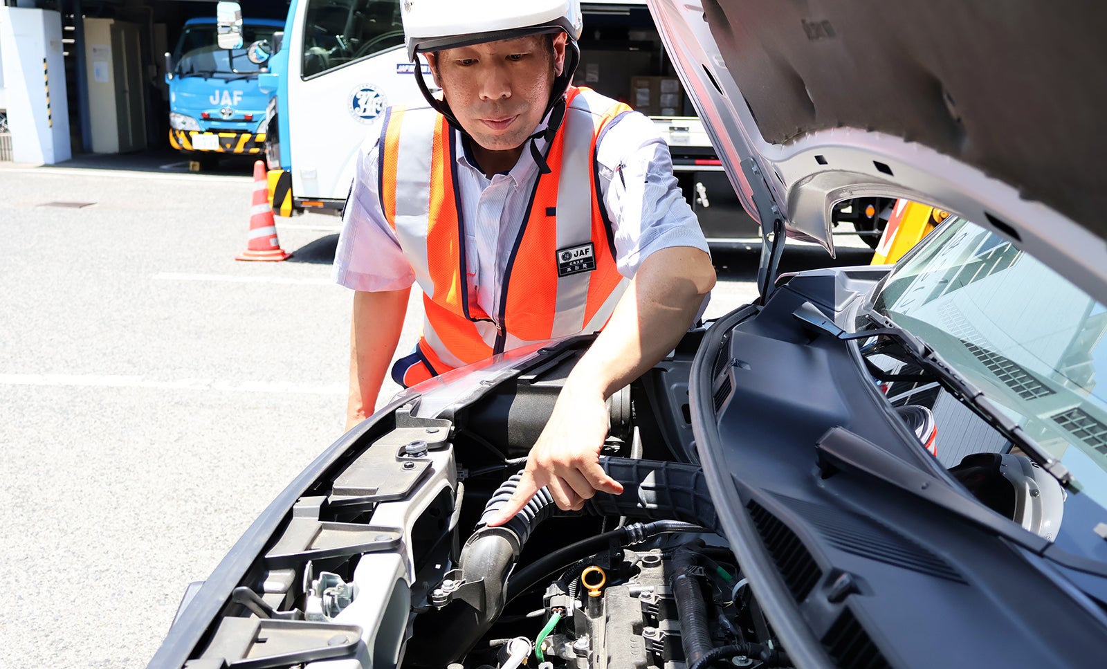 エンジンルーム内にあるエアインテークを指さす高田隊員