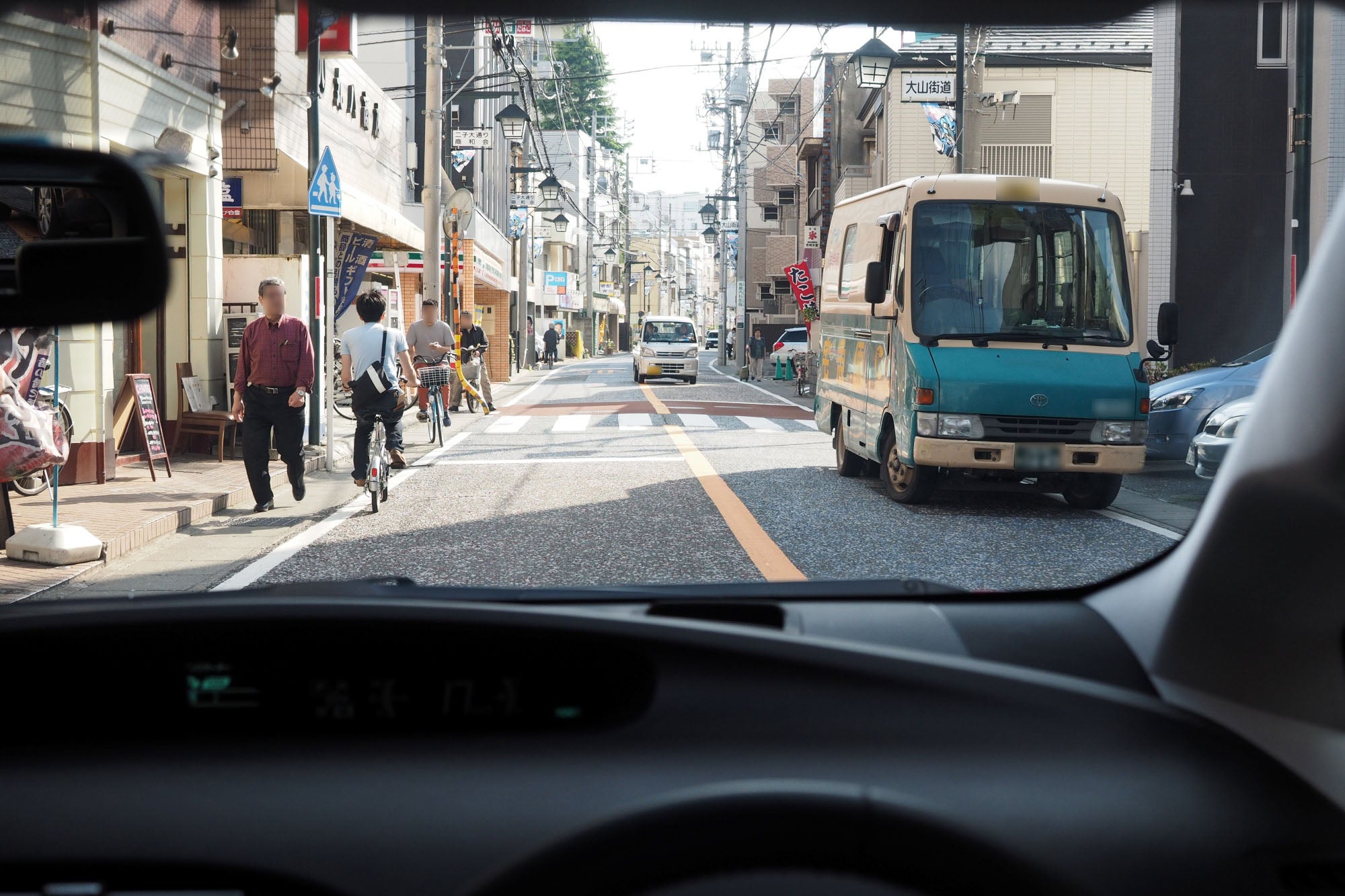 自転車や歩行者が行き交う商店街の通りを通行する自車