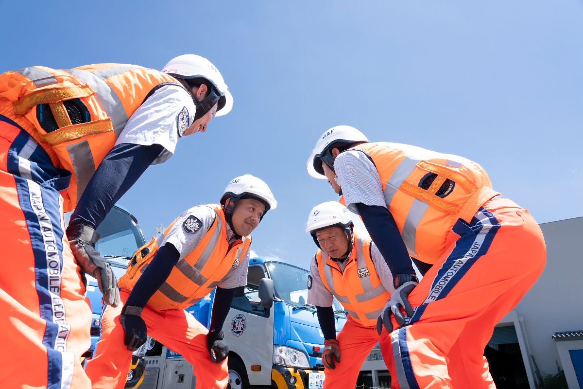 JAF全国ロードサービス競技大会2025 関西本部代表選手｜オレンジ色の作業服とヘルメット姿の隊員4名が青空の下でトラック前に集合