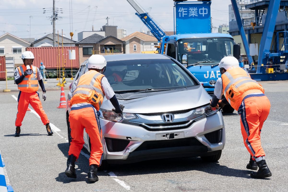 JAF全国ロードサービス競技大会2025 関西本部代表選手｜駐車場でシルバーの車を押す隊員とJAFのレッカー車、作業中の看板