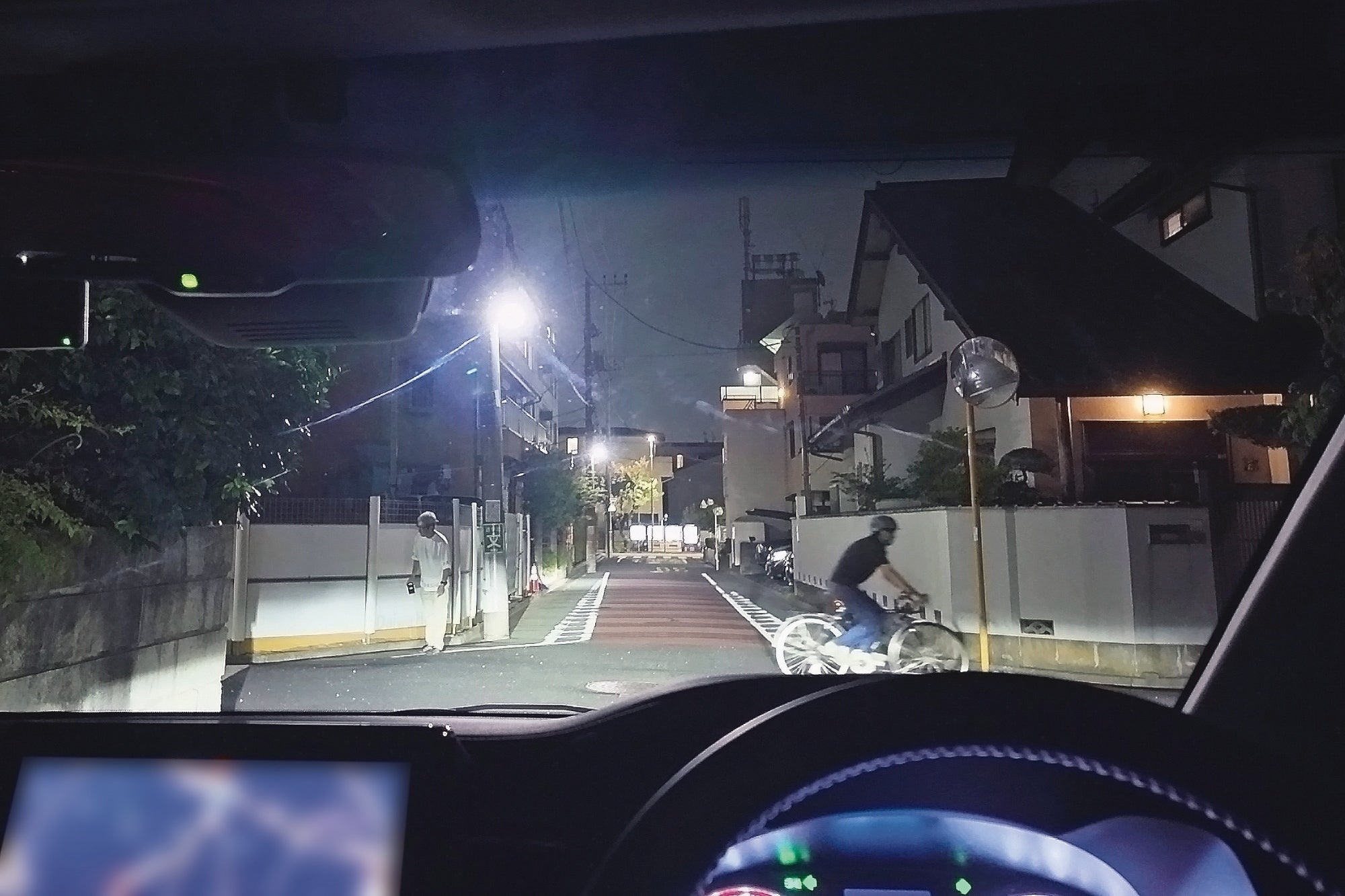 夜間に住宅街の交差点を通行する自車と前を横切る自転車
