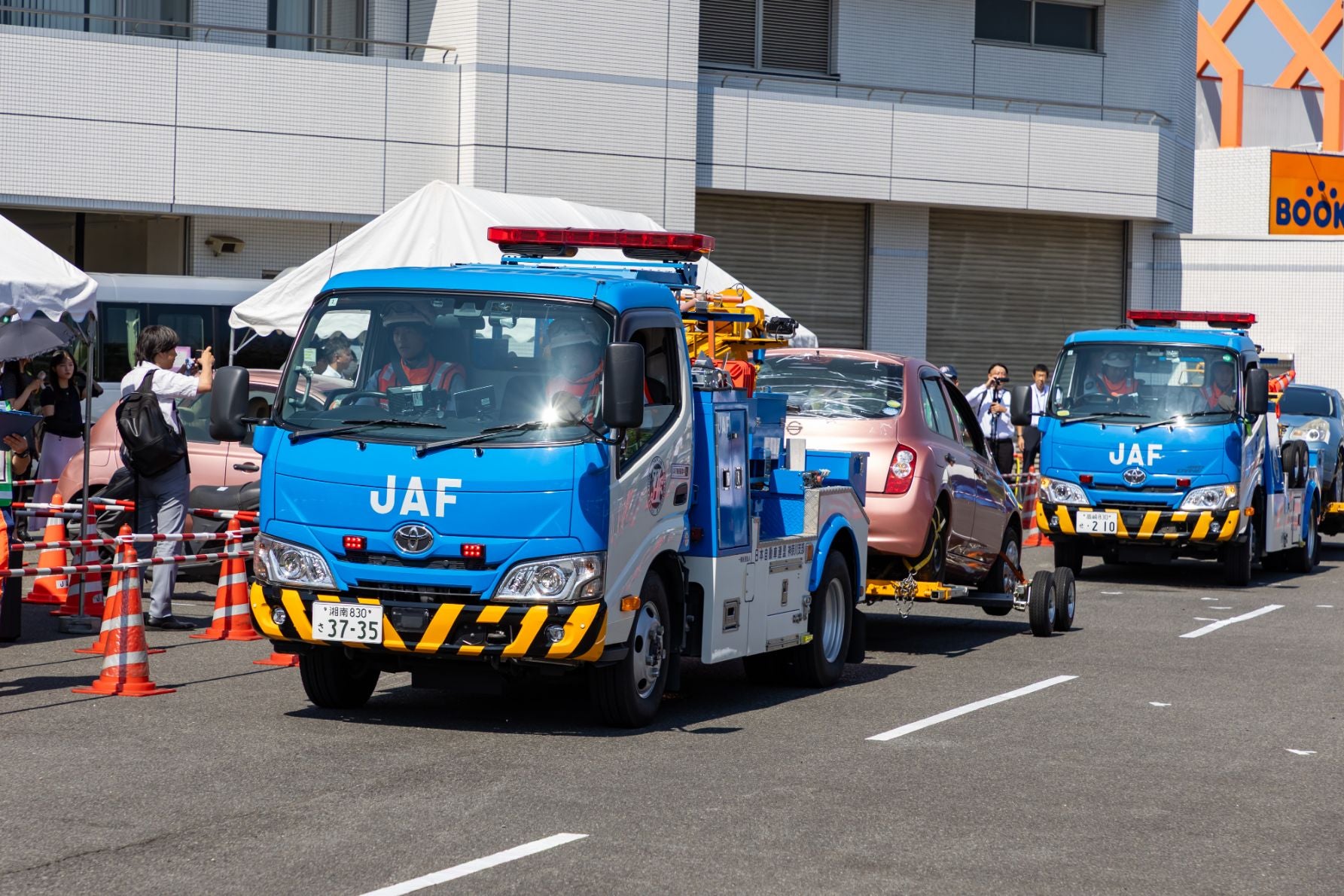 JAFの青いレッカー車2台が車両をけん引している様子。周囲には三角コーンやテントが見える