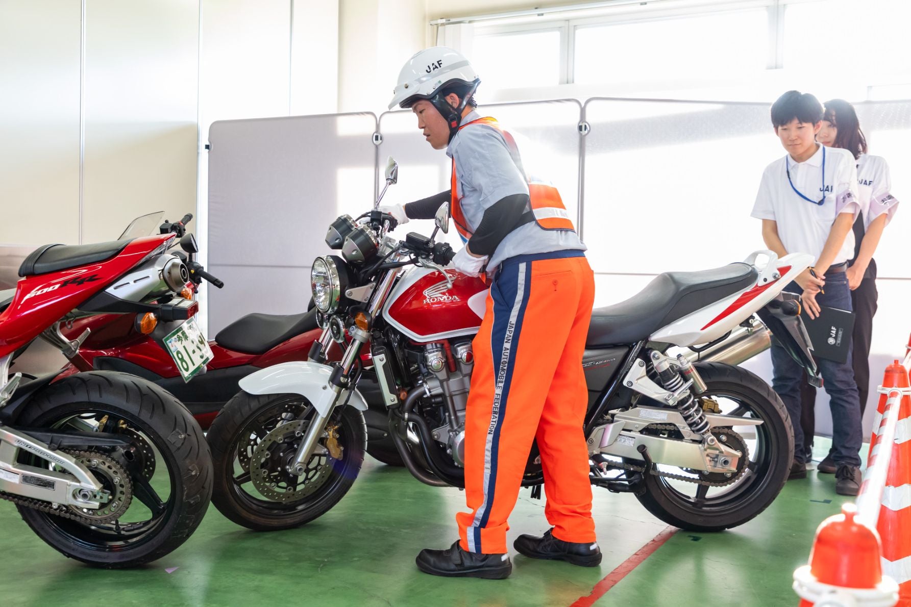 内でJAFスタッフが赤白のバイクを操作し、他のスタッフが見守っている競技の様子