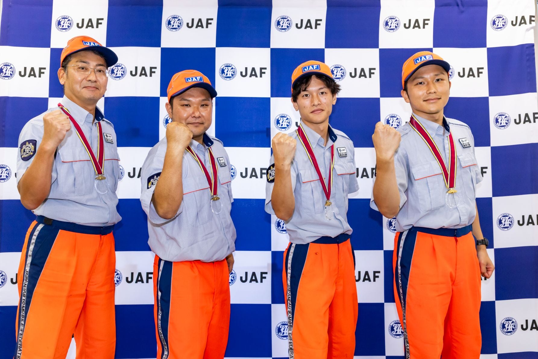  JAFのロゴが入った背景の前で、ユニフォームとメダルを着用した九州本部の選手4人が拳を掲げてポーズを取っている