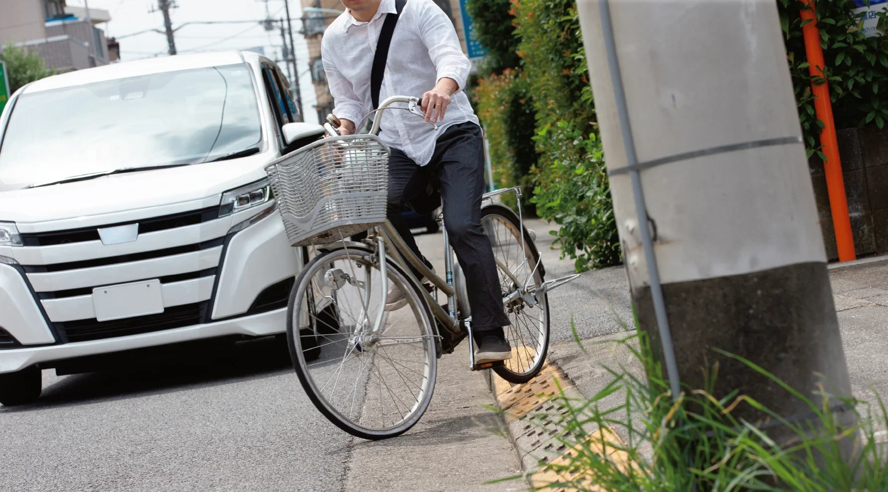 歩道から車道に自転車が降りてくる様子。その後方には白いミニバンが通っている