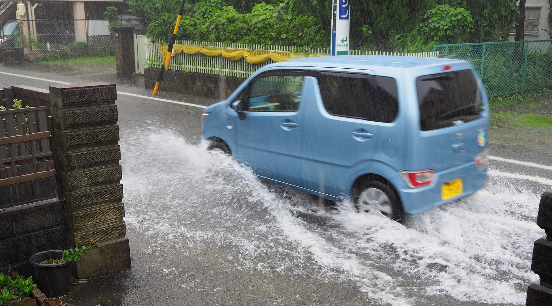冠水した道路を、水をはねながら走る軽自動車