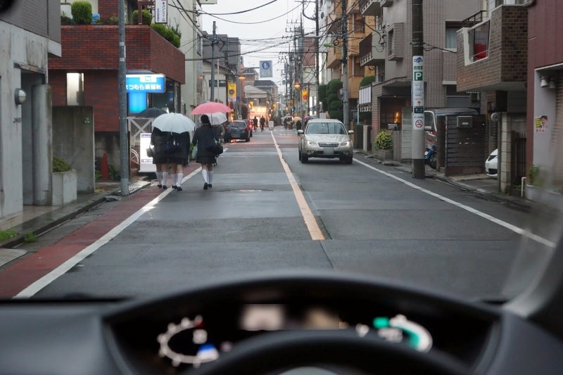 雨の住宅街を行き交う歩行者と対向車