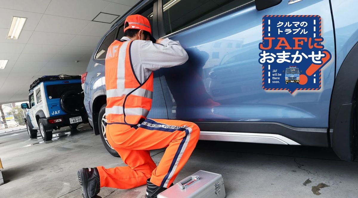 JAFの隊員が、鍵をインロックしたと思われる車の横にひざまずき、鍵を開ける作業をしています。工具箱が置かれています。右上の広告スペースには「クルマのトラブル JAFにおまかせ」の文字が書かれています