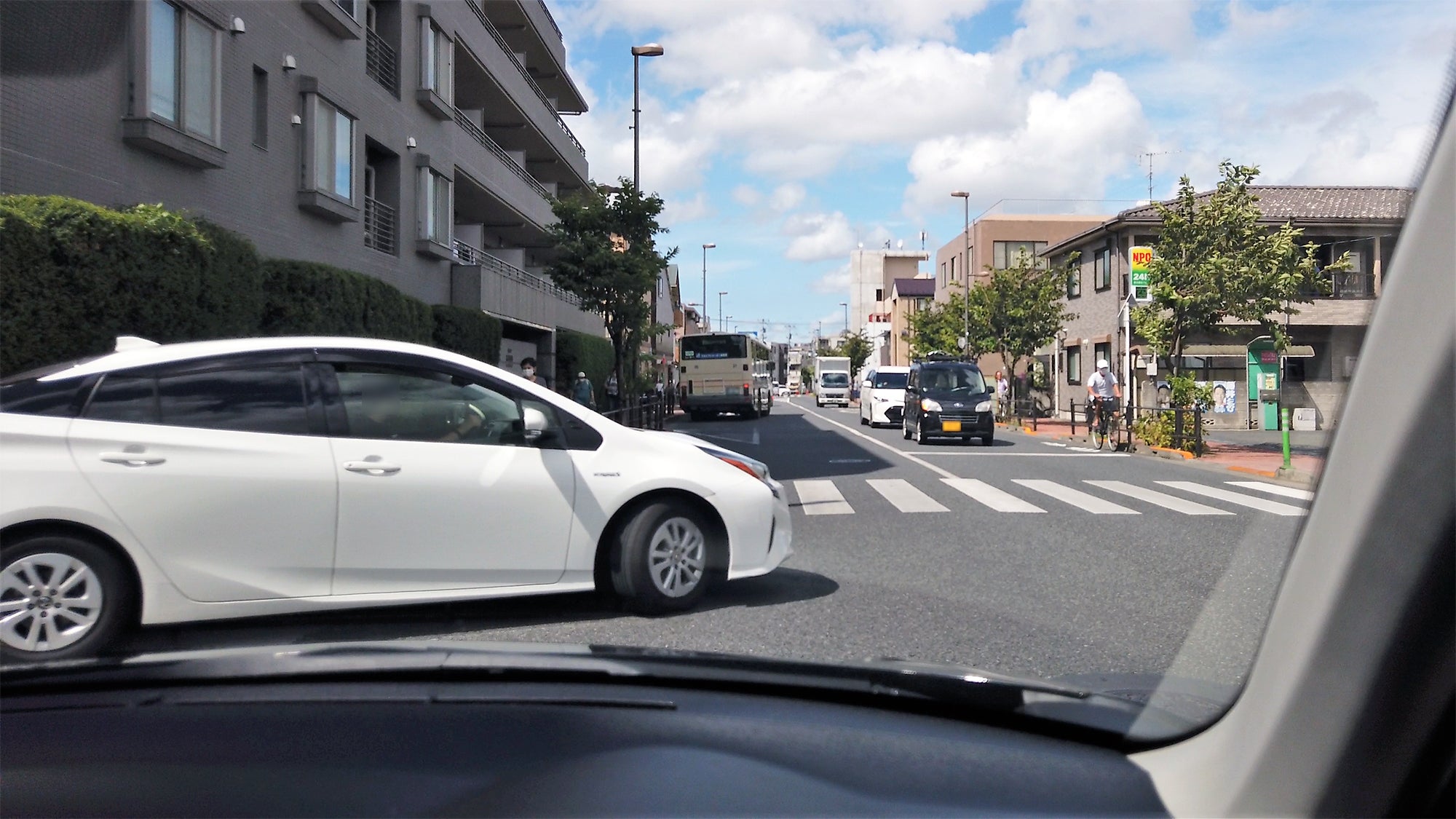 狭い道路から白い車が出た後に左折しようとする自車